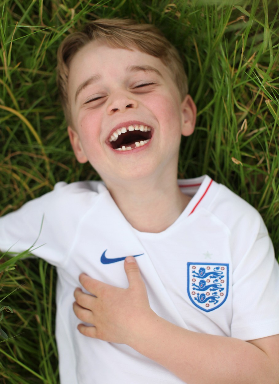 Prințul George în timp ce stă întins pe iarbă și râde