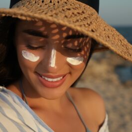O femeie care stă cu o pălărie de soare pe cap și are aplicată pe față cremă de protecție solară