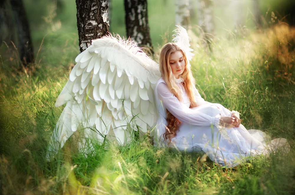 Femeie în rochie albă, în pădure, cu pene de înger pe spate
