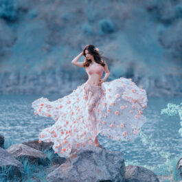 Fată frumoasă îmbrăcată într-o rochie de voal stă aproape de apă
