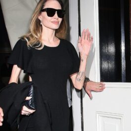 Îmbrăcată în haine negre și ochelari de soare clasci, negri, Angelina Jolie zâmbește și îi salută pe jurnaliștii care o așteptau la ieșirea din hotelul NYC pe 18 august 2023
