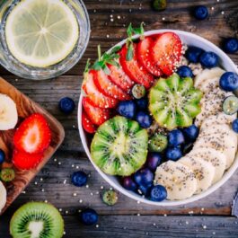O imagine în care apare un mic dejun sănătos care cuprinde un bol cu terci de ovăz, felii de banană, kiwi, căpșune, afine și semințe de chia