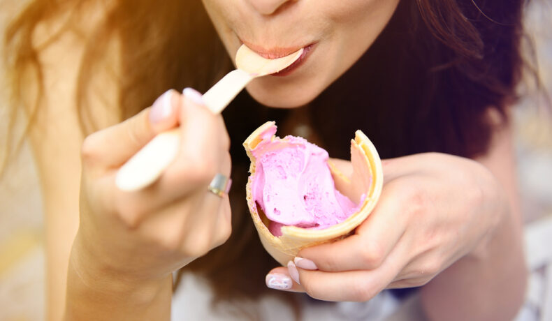 O femeie care consumă înghețată de căpșuni cu lingurița dintr-un cornet