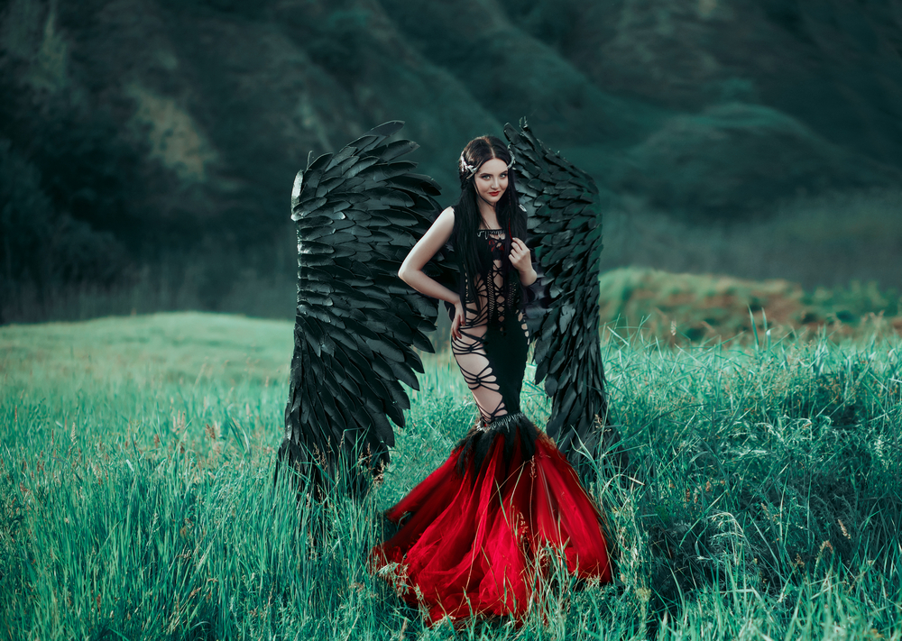 O tânără brunetă, îmbrăcată într-o rochie neagră cu roșu, croită în stilul sirenă. Ea are aripi negre de înger.