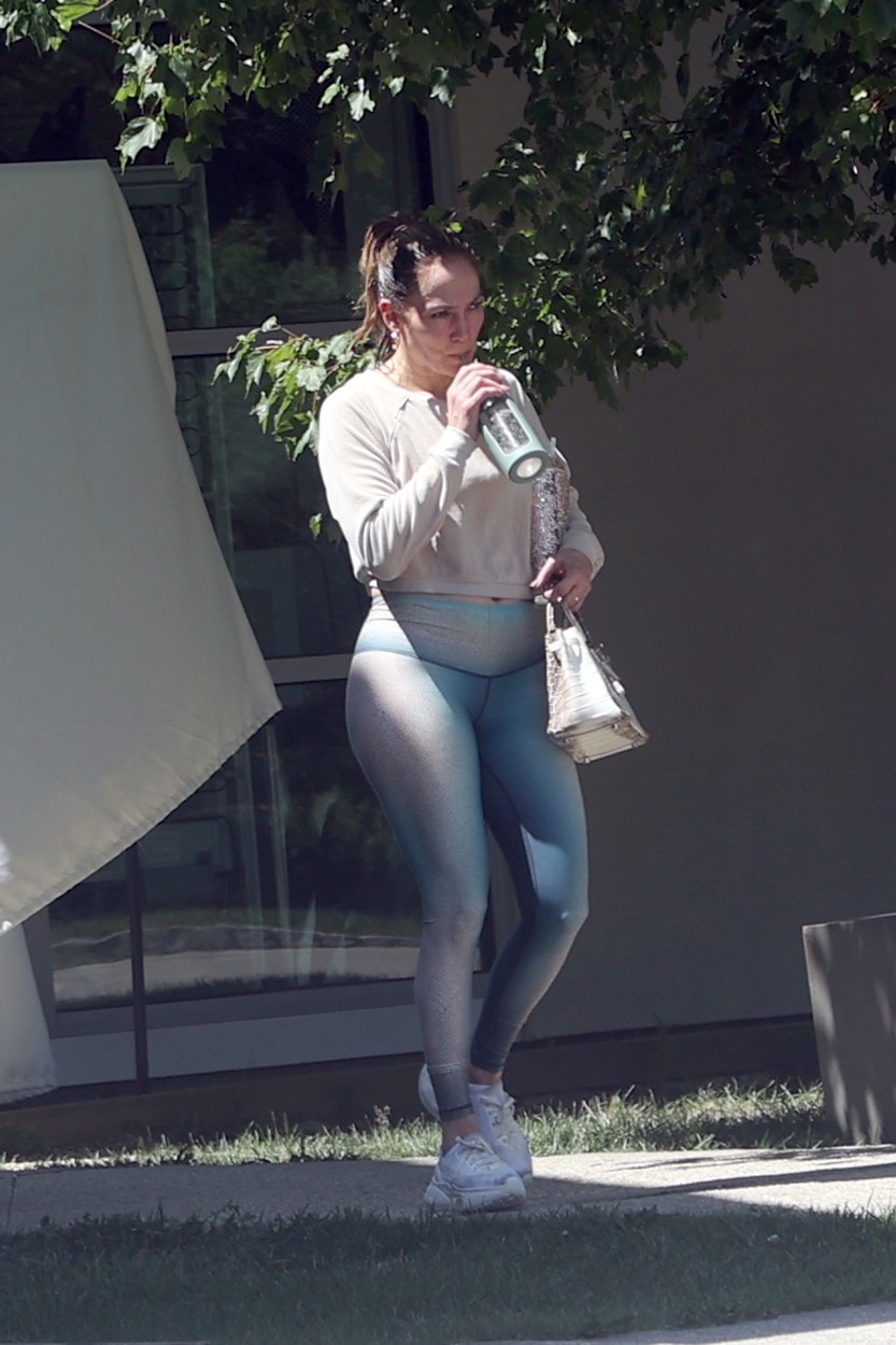 Îmbrăcată într-o ținută sport, Jennifer Lopez bea apă dintr-un pahar înainte să traverseze o stradă din The Hamptons, statul New York
