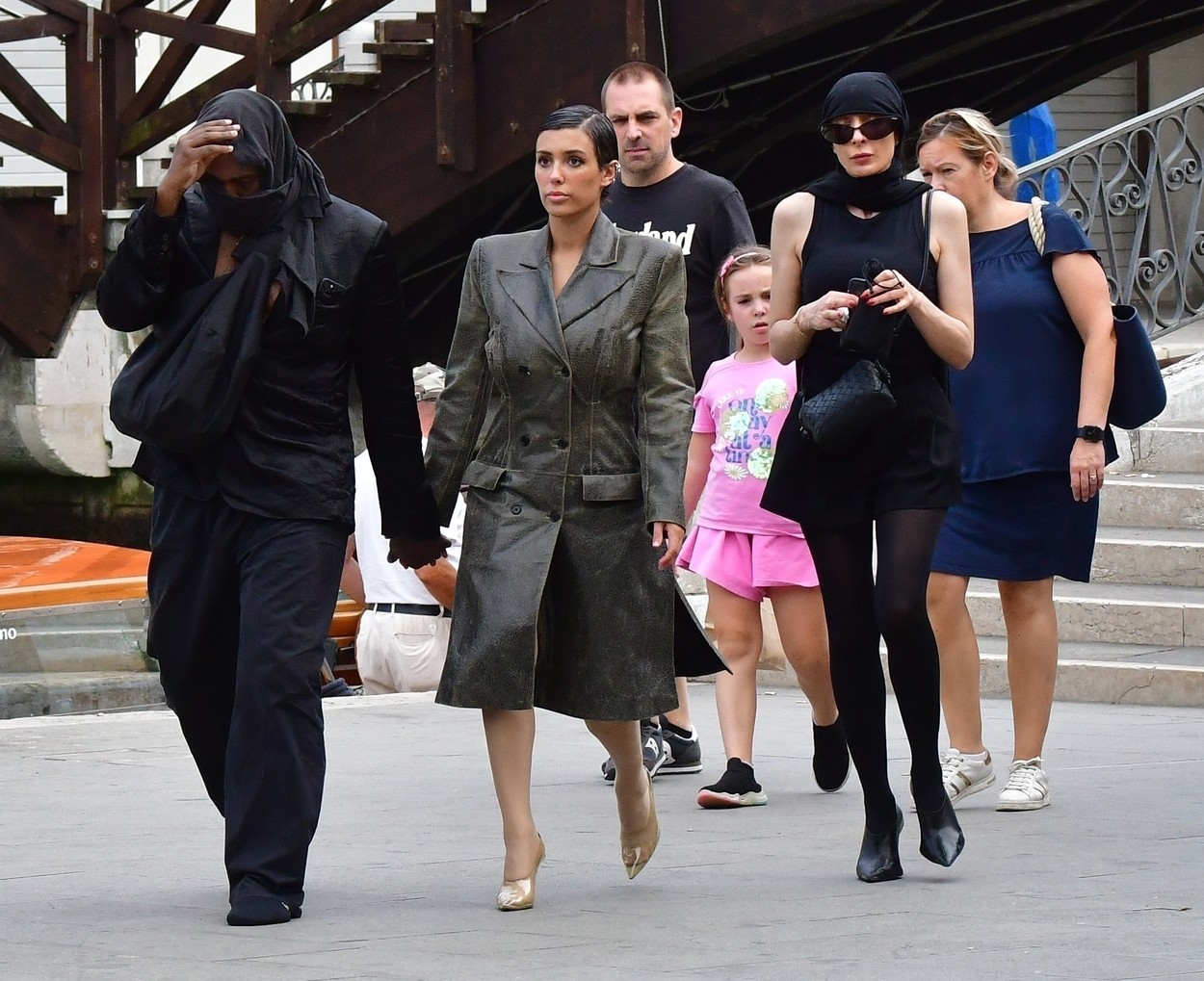 Încălțat doar cu șosete, Kanye West a purtat haine negre și și-a acoperit fața cu o eșarfă, în timp ce Bianca Censori avea o haină neagră de piele și pantofi transparenți cu toc