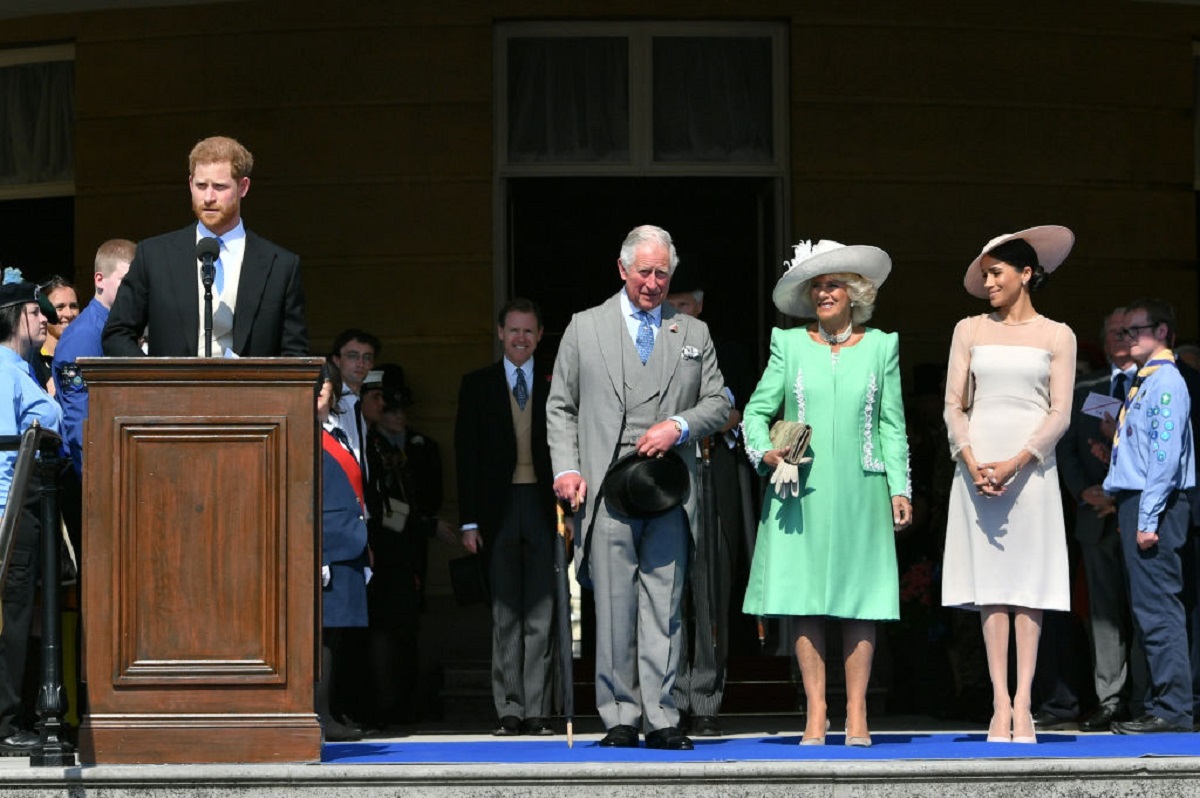 Prince Harry se află la pupitrul pus pentru un eveniment din 22 mai 2018, la care au participat tatăl său, soția acestuia și Meghan Markle