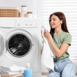O femeie frumoasă care stă lângă mașina de spălat și curăță prosoapele