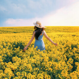 Fată frumoasă într-un câmp de flori cu o pălărie de soare pe cap