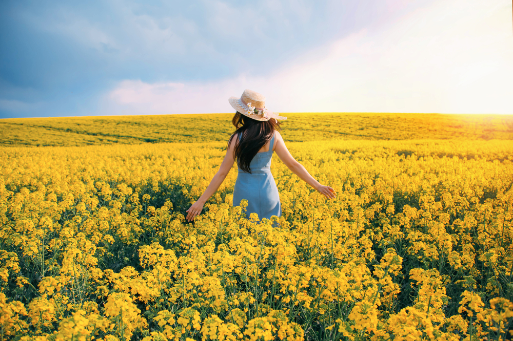 Fată frumoasă într-un câmp de flori cu o pălărie de soare pe cap