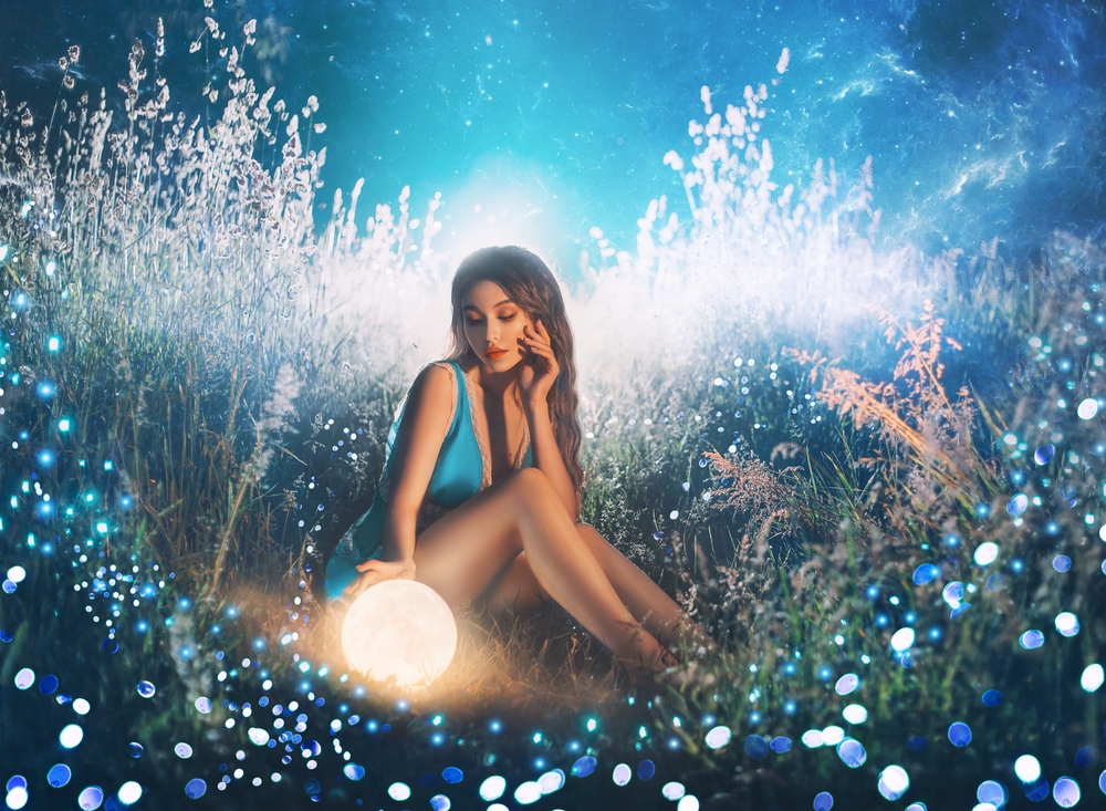 Fată frumoasă stă în iarbă cu o lampă de veghe în formă de lună