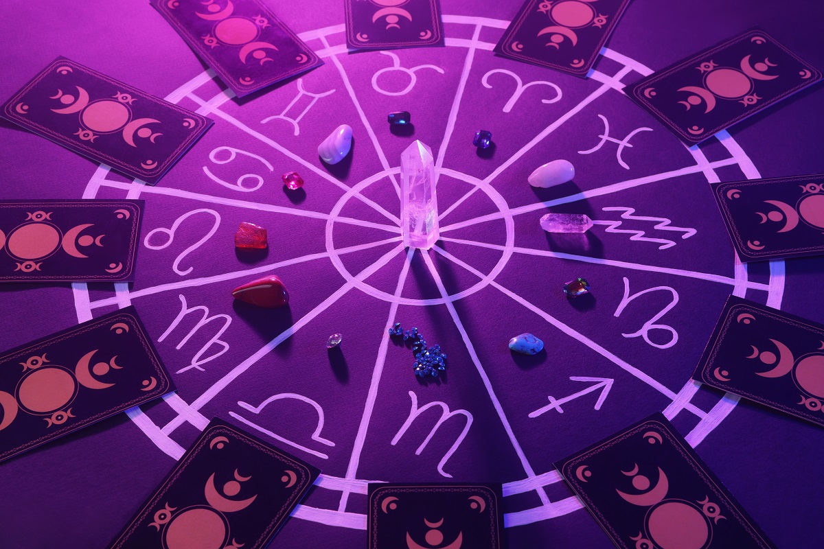 Harta astrală cu nativii din zodiac, cristale și cărți de tarot, toate aranjate pe o tablă violet