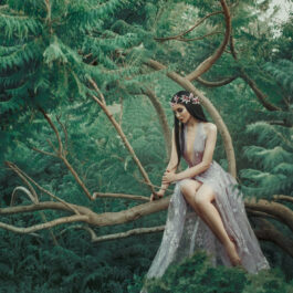 Fată frumoasă îmbrăcată într-o rochie de voale stă într-o pădure