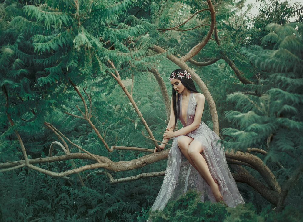 Fată frumoasă îmbrăcată într-o rochie de voale stă într-o pădure