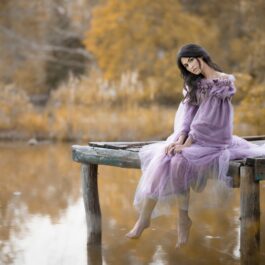 O femeie frumoasă, care poartă o rochie mov și stă pe marginea unui lac, reprezentând zodia nefericită a lunii septmebrie 2023