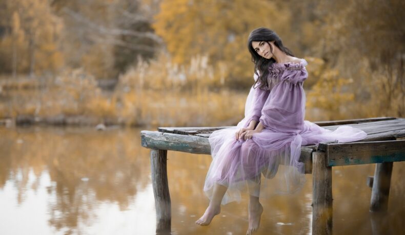 O femeie frumoasă, care poartă o rochie mov și stă pe marginea unui lac, reprezentând zodia nefericită a lunii septmebrie 2023