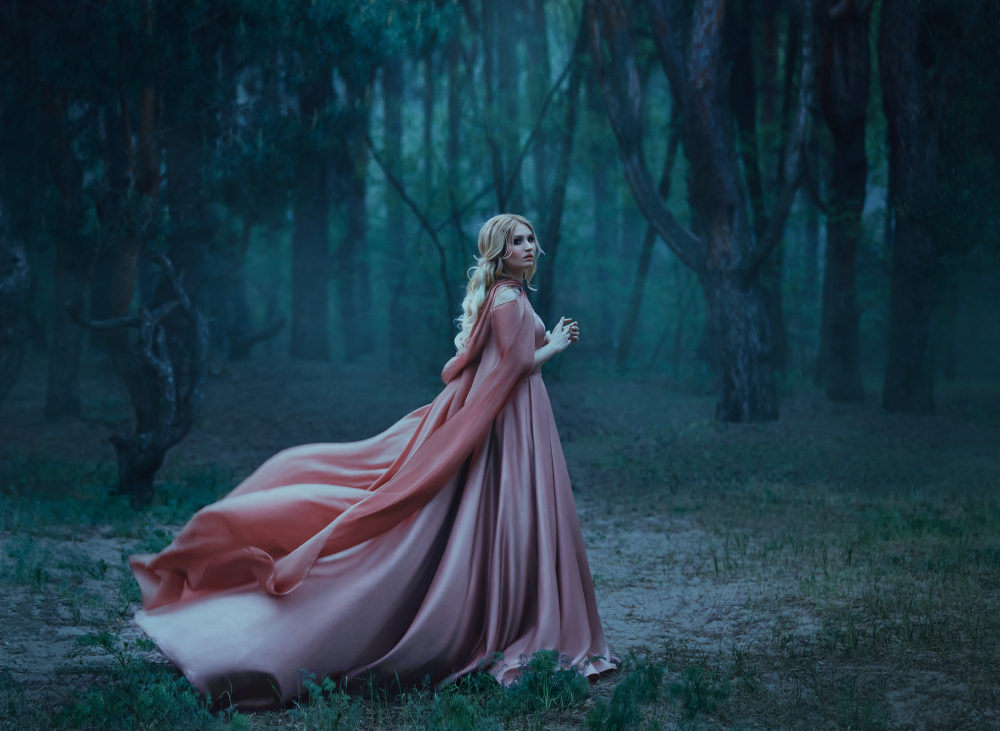 Fată frumoasă blondă îmbrăcată într-o rochie lungă, roz stă într-o pădure
