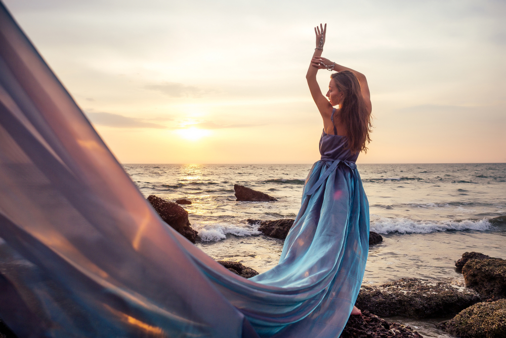Fată frumoasă îmbrăcată într-o rochie de voal stă cu fața spre soare