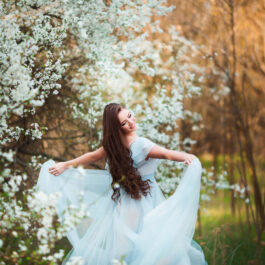Fată frumoasă îmbrăcată într-o rochie albă stă într-o pădure
