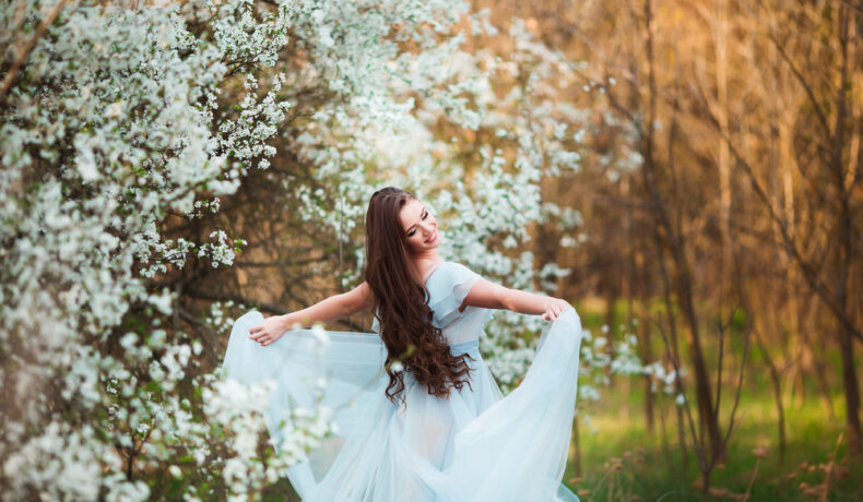 Fată frumoasă îmbrăcată într-o rochie albă stă într-o pădure