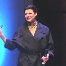 Linda Evangelista, într-un palton negru, cu ochelari în mână, la un eveniment