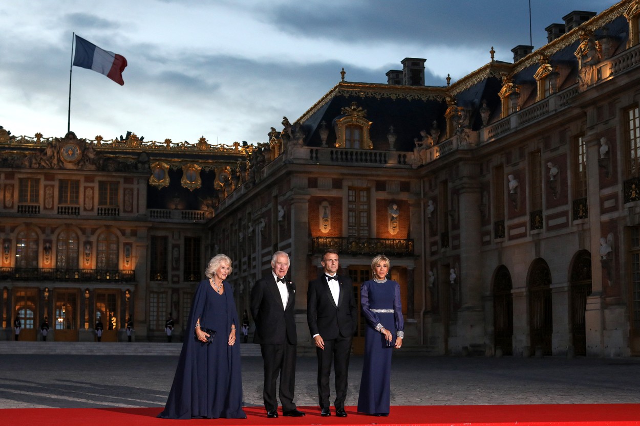 Regele și Regina Marii Britanii și Președintele Franței cu soția sa, îmbrăcați elegant, în fața Palatului Versailles