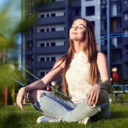 O tânără care stă pe iarbă și se bucură de razele Soarelui