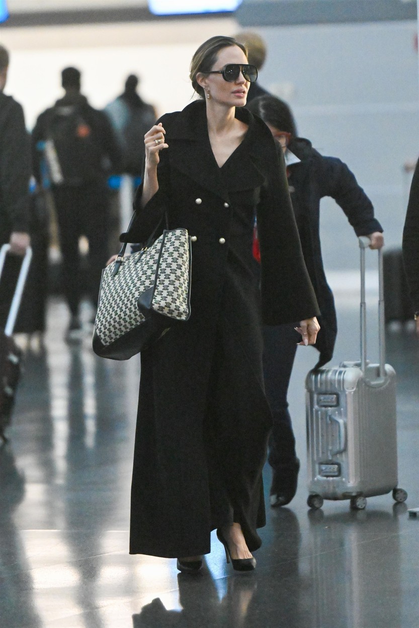 Angelina Jolie, într-un trenci negru, cu o geantă mare, de brand, în aeroport