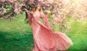 Fată frumoasă îmbrăcată într-o rochie roz stă într-o grădină plină cu flori