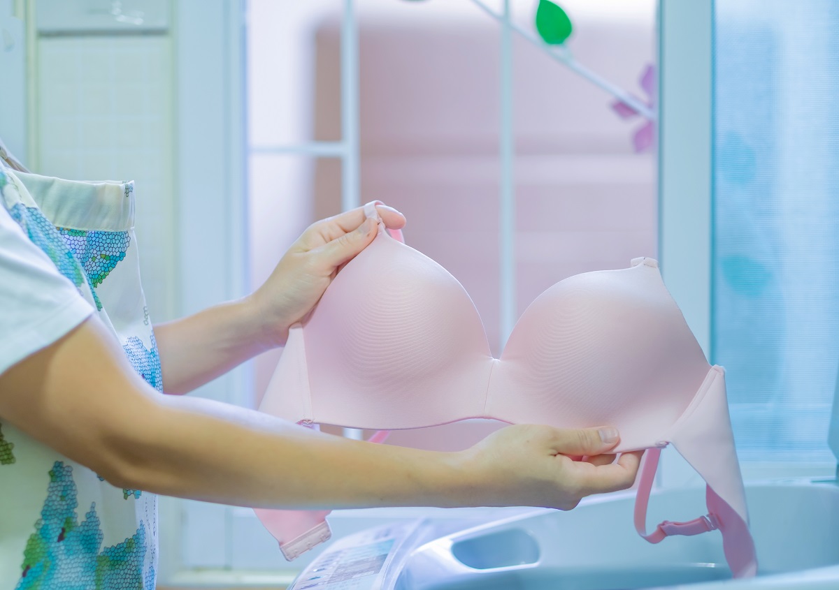 O femeie frumoasă care își spală sutienul roz pentru a ilustra cât de des e recomandat să-ți speli sutienul