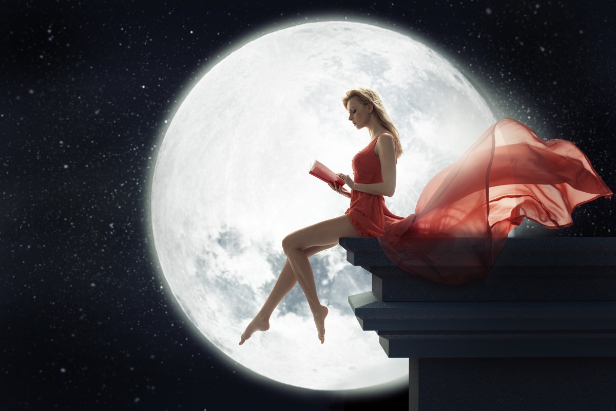 O femeie frumoasă care poartă o rochie roșie și citește pentru a ilustra ce e recomandat să faci atunci când este Lună Nouă
