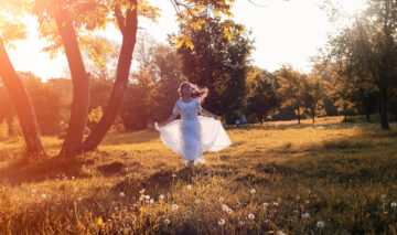 Fată frumoasă îmbrăcată în alb aleargă pe un câmp