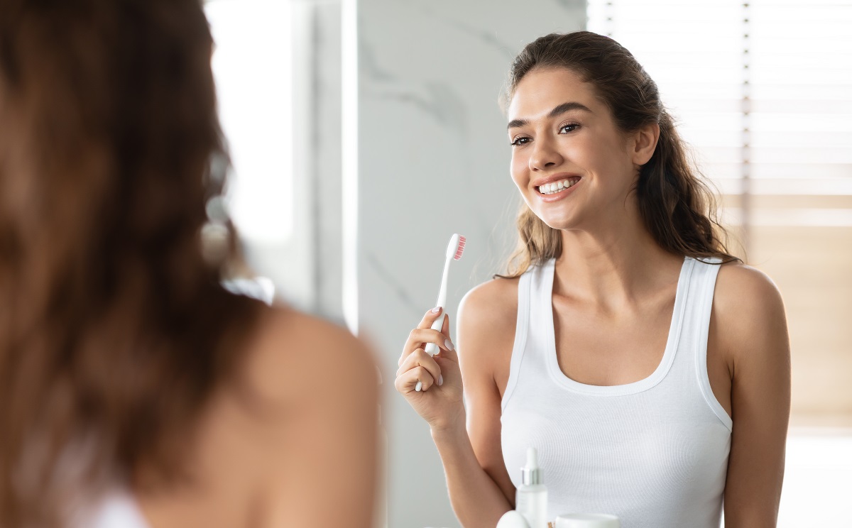 O femeie frumoasă care se periază pe dinți și se admiră în oglindă