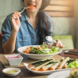 O femeie care stă la masă și mănâncă pentru a ilustra motivul pentru care ți se face foame des