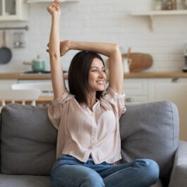 O femeie frumoasă care stă pe o canapea și se întinde pentru a ilustra obiceiul la care e indicat să renunți dacă vrei să ai mai multă energie