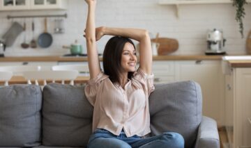O femeie frumoasă care stă pe o canapea și se întinde pentru a ilustra obiceiul la care e indicat să renunți dacă vrei să ai mai multă energie