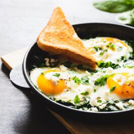 O farfurie plină cu două ouă ochiuri cu brânză feta și servite cu o felie de pâine