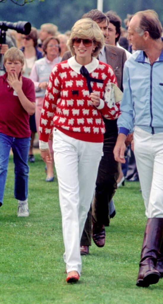 Prințesa Diana, la un joc de polo, într-un pulover roșu cu oi albe și o oaie neagră și blugi albi