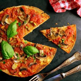 Rețeta de pizza care nu îngrașă ilustrată cu ajutorul unei pizze mari alături de care se află o felie tăiată, un cuțit și o fruculiță