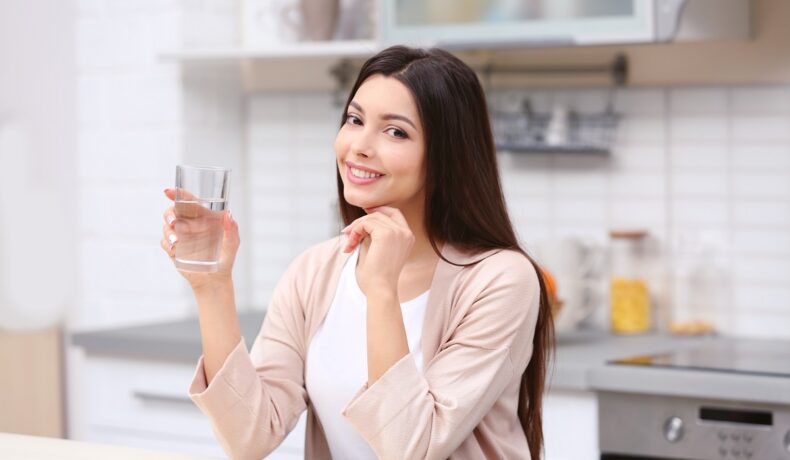 O femeie frumoasă care ține în mână un pahar de apă pentru a ilustra semnele care îți arată deshidratarea organismului