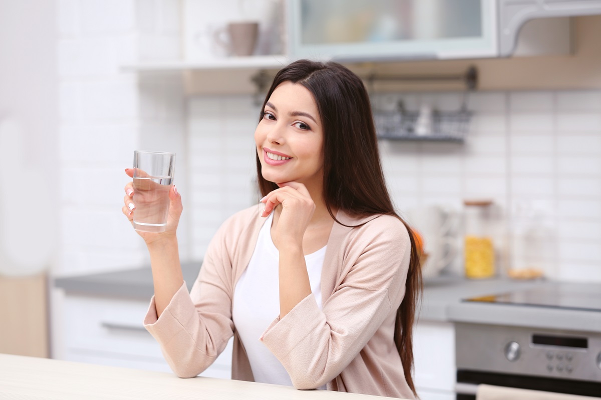 O femeie frumoasă care ține în mână un pahar de apă pentru a ilustra semnele care îți arată deshidratarea organismului