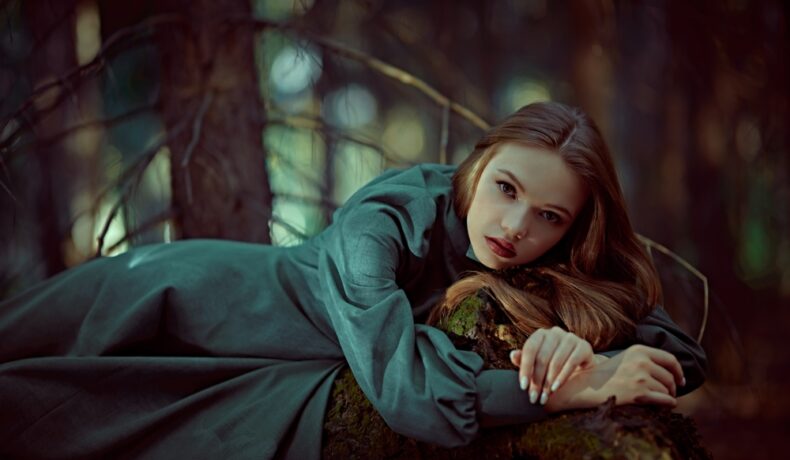 Fată frumoasă îmbrăcată într-o rochie verde lungă stă într-o pădure