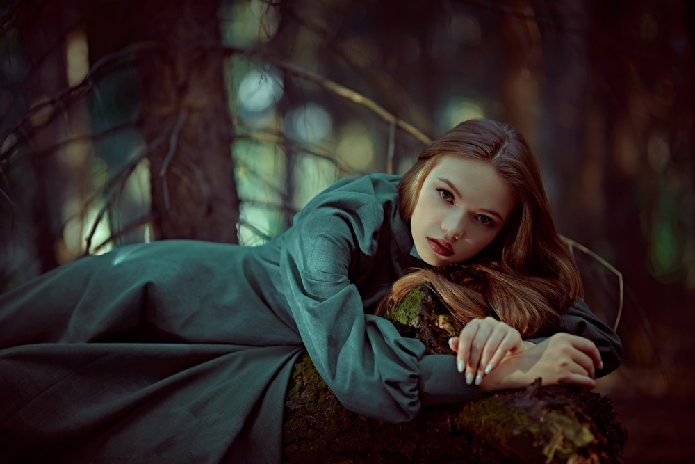 Fată frumoasă îmbrăcată într-o rochie verde lungă stă într-o pădure