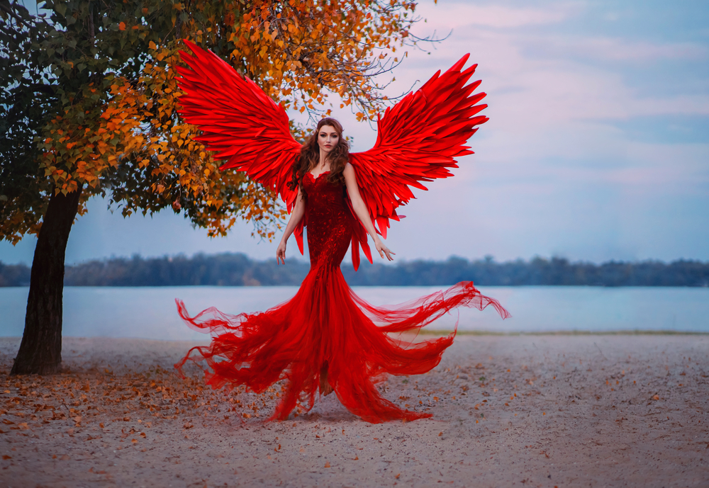 O femeie frumoasă, în câmp deschis, îmbrăcată într-o rochie roșie cu aripi roșii