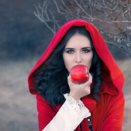 Fată frumoasă îmbrăcată într-o pelerină roșie mănâncă un măr