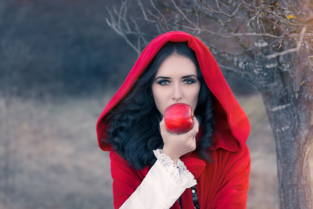 Fată frumoasă îmbrăcată într-o pelerină roșie mănâncă un măr