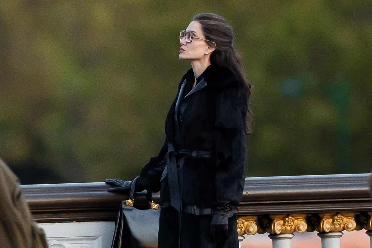 Angelina Jolie, într-o haină de culoare neagră, cu ochelari supradimensionați, în timp ce se află la filmări