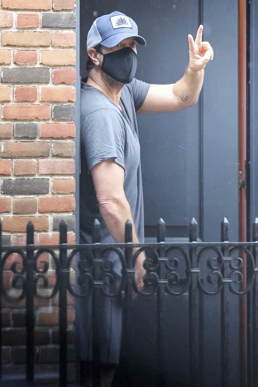 David Schwimmer cu o mască pe față și o șapcă pe cap în timp ce le face cu mâna fanilor care îl așteaptă în fața casei