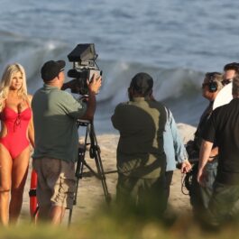 Donna D'Errico într-un costum de baie roșu în timp ce filmează pe o plajă pentru serialul Baywatch