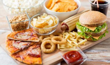 Un blat pe lemn pe care se află mai multe produse de tip fast food pentru a ilustra câteva alimente și băuturi care afectează sănătatea oaselor